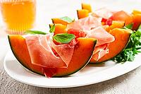Cantaloupe melon with prosciutto and fresh basil, on a white plate, natural light [IBR124552196]