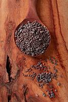 Crystals of black salt, on a wooden spoon, laid out on a wooden surface, top view [IBR124552201]