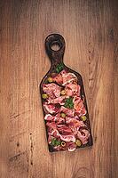 Assortment, sliced meat appetizer, prosciutto, salami and ham, with olives, on a wooden board, breakfast, top view, close-up, no people [IBR124552208]