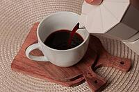 Freshly brewed coffee is being carefully poured from a stovetop coffee maker into a small white cup, resting on a wooden cutting board, creating a cozy atmosphere [IBR124552225]