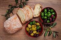 A mixture of olives, varieties of Halkidiki, Verdi giganti and Kalamata, in a bowl, with sliced ciabata bread, top view, no people [IBR124552231]