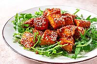 Fried salmon slices, teriyaki with sesame seeds, with arugula salad, top view [IBR124552233]
