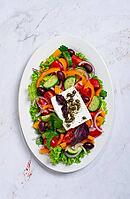 This dish features a salad made with a mix of lettuce, peppers, cucumbers, red onion, and olives. It is topped with feta cheese and capers [IBR124552235]