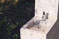 This outdoor sink features a sleek terrazzo design, with a shiny faucet and a simple drain. It is situated in a landscaped garden, bathed in warm sunlight [IBR124552247]