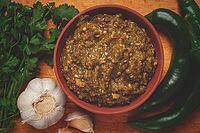 Green adjika, in a clay bowl, Georgian sauce, with ingredients on a wooden board, top view, no people [IBR124552250]