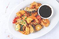 Shrimp and assorted vegetables are deep fried in a light batter and served on a white plate. A small bowl of soy sauce is beside the dish [IBR124552253]