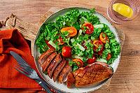 Delicious grilled duck breast served with fresh garden salad and cherry tomatoes at a rustic dining table [IBR124585337]
