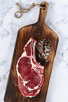 Raw rib eye steak, cowboy steak, wooden chopping board, marble table, top view, no people [IBR124585354]