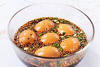 Five soft boiled eggs sit in a bowl filled with soy sauce, chopped green onions, and sesame seeds [IBR124585357]