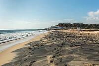 Wide sandy beach in Quarteira, Algarve, Portugal with visible footprints leading along the shoreline and gentle waves of the Atlantic Ocean. Peaceful coastal scene with clear blue sky, natural light, and distant buildings, ideal for travel and seaside con [IBR124586572]