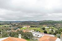 Panoramic view of São Marcos da Serra, a quiet rural village in the Algarve interior of Portugal, featuring traditional white houses, rolling green hills, and a cloudy sky [IBR124586591]