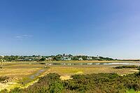 Scenic view of a tranquil coastal lagoon in Quinta do Lago, Algarve, Portugal, featuring shallow waters, natural vegetation, and wading birds under a clear blue sky [IBR124586604]
