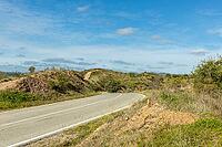 Scenic countryside road leading to Moinho das Amendoeiras in the Algarve, Portugal, surrounded by rolling hills, green landscape, and blue sky with clouds [IBR124586617]