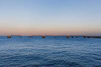 Peaceful seascape with gentle waves and a long pier stretching into the ocean at sunset in Lisbon, Portugal. Soft pastel sky and tranquil coastal atmosphere create a minimalist travel scene [IBR124586618]