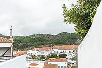Panoramic view of São Marcos da Serra, a quiet rural village in the Algarve interior of Portugal, featuring traditional white houses, rolling green hills, and a cloudy sky [IBR124586621]