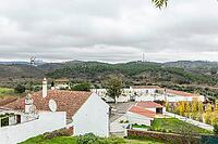 Panoramic view of São Marcos da Serra, a quiet rural village in the Algarve interior of Portugal, featuring traditional white houses, rolling green hills, and a cloudy sky [IBR124586627]