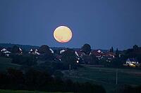 Full moon red silver moon in front of houses and blue sky, Herrnwahlthann, Bavaria, Germany [IBR124586659]