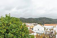 Lemon tree in the foreground with a view over São Marcos da Serra, a traditional village in the Algarve interior of Portugal, surrounded by hills, white houses, and cloudy skies [IBR124586663]