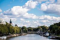 Turku, Finland - August 30, 2014 - Sunny riverfront scene with boats and bridge under cloudy blue sky [IBR124626852]
