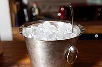 A metal bucket filled with ice cubes sits on a wooden countertop, with a kitchen background. perfect for refreshing drinks or parties, it adds a touch of chill to indoor gatherings [IBR124626866]