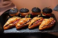 A delicious arrangement of gourmet croissants filled with ham and cheese, alongside unique black burgers featuring fresh ingredients, presented on a slate platter [IBR124626872]