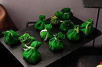 A selection of green pastry bites elegantly presented on a dark tray. these appetizing treats are wrapped and tied, adding a touch of sophistication to any culinary display [IBR124626873]