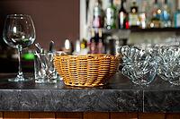 A stylish display of bar essentials on a dark countertop, featuring a wicker basket flanked by glassware and utensils. a glimpse of a well-stocked bar adds a touch of sophistication [IBR124626878]