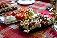 A beautifully arranged platter featuring an assortment of cheeses, fresh vegetables, and grapes. ideal for gatherings or parties, this setup combines color and flavor on a vibrant tablecloth [IBR124626880]