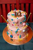 A vibrant two-tiered cake adorned with colorful polka dots and playful curly ribbons, topped with a golden number ten. perfect for a joyous tenth birthday celebration [IBR124626882]