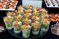 A sophisticated arrangement of appetizers in individual glasses, featuring a mix of fresh ingredients like greens, mini eggs, and toppings. ideal for catering events and sophisticated gatherings [IBR124626884]