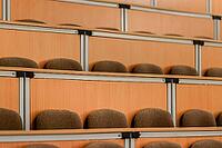 A spacious lecture hall featuring rows of empty, cushioned wooden seats. the arrangement provides a sense of order and anticipation, capturing the essence of academic settings [IBR124626894]