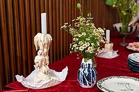 A stylish table setup featuring a tall candle with melted wax on a red cloth. a bouquet of white flowers in a blue vase adds a touch of charm to the scene [IBR124626914]