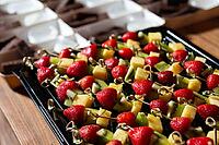 A vibrant display featuring skewers of fresh strawberries, kiwi, and pineapple, accompanied by chocolate desserts in the background. perfect for parties or gatherings [IBR124626918]