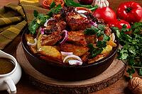 Ojakhuri, fried meat with potatoes, in ketsi, on a wooden table, Georgian cuisine, against a background of fresh ingredients [IBR124629125]