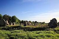This atmospheric picture shows the famous stone rows of Carnac in Brittany. Numerous Neolithic menhirs rise from the grass and lead the eye to a characteristic stone house. The low sun bathes the scene in golden light and accentuates the rough granite tex [IBR124629132]