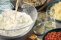 Milk is poured into a bowl of flour, surrounded by other cooking ingredients [IBR124636276]