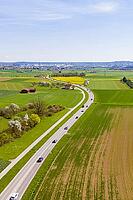 A country road runs through green fields under a clear blue sky, past blooming trees, Aidlingen, Böblingen district, Germany [IBR124642845]