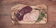 Fresh raw duck breasts, on a wooden chopping board, with herbs and spices, no people [IBR124748949]