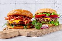 Two burgers with beef patty, fried bacon, cheddar cheese, tomatoes, on a light table [IBR124748953]