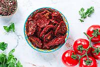 Dried tomatoes, in a ceramic bowl, with fresh herbs and spices, on a white marble surface, top view, no people [IBR124748958]
