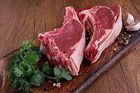 Freshly sliced lamb chops, with herbs and vegetables, on a wooden board, ready to cook, on a wooden table [IBR124748961]