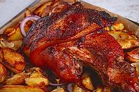 Baked pork knuckle, with potato slices, on a tray, with red sauce, homemade, no people, light background [IBR124748970]