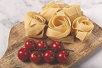 Raw pappardelle pasta, on a wooden chopping board, with cherry tomatoes, top view, no people [IBR124748972]
