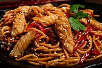 Udon noodles, with squid and vegetables, on a black plate, homemade, no people [IBR124748977]