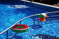 A colorful ball and an inflatable circle, with a watermelon pattern floating. in a sunny outdoor pool on a summer day, there are no people [IBR124748992]