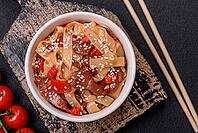 Food, Delicious asian udon dish with vegetables, meat, salt and spices on a ceramic plate on a dark concrete background [IBR124773704]