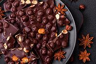 Food, Black bitter chocolate with whole hazelnuts, candied fruits and mint, broken into pieces on a dark concrete background [IBR124773710]