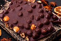 Food, Black bitter chocolate with whole hazelnuts, candied fruits and mint, broken into pieces on a dark concrete background [IBR124773711]