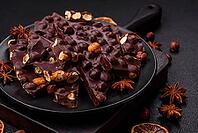 Food, Black bitter chocolate with whole hazelnuts, candied fruits and mint, broken into pieces on a dark concrete background [IBR124773712]