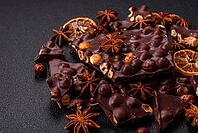Food, Black bitter chocolate with whole hazelnuts, candied fruits and mint, broken into pieces on a dark concrete background [IBR124773713]